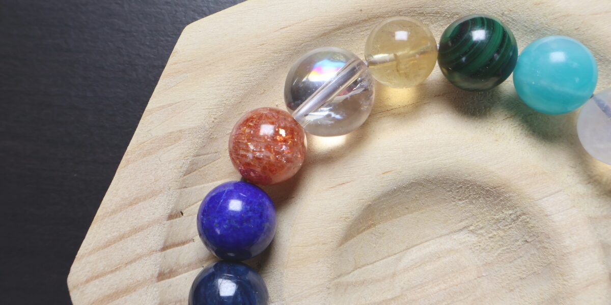 木製のトレイに置かれた、サンストーン、水晶、シトリン、マラカイト、ラピスラズリなどカラフルな天然石を組み合わせた推し活ブレスレット